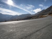 a motorcycle driving along a winding road through a valley to mountains and peaks in the background