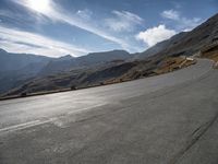 a motorcycle driving along a winding road through a valley to mountains and peaks in the background