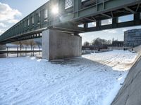 a bridge over a body of water with some snow on the ground under it next to the sidewalk