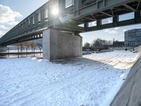 a bridge over a body of water with some snow on the ground under it next to the sidewalk