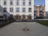 a courtyard that has benches, a fence and buildings in the background on a sunny day