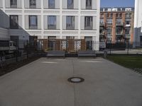 a courtyard that has benches, a fence and buildings in the background on a sunny day