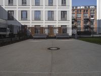 a courtyard that has benches, a fence and buildings in the background on a sunny day