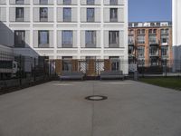 a courtyard that has benches, a fence and buildings in the background on a sunny day