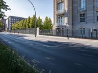 an empty street lined with a long building and many trees in the distance on a sunny day