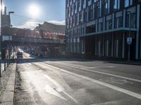 an empty street is visible in the morning sunshine with traffic driving along it and many buildings