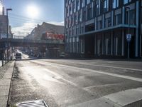 an empty street is visible in the morning sunshine with traffic driving along it and many buildings