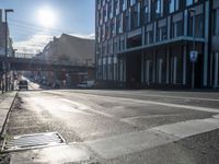 an empty street is visible in the morning sunshine with traffic driving along it and many buildings