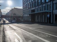 an empty street is visible in the morning sunshine with traffic driving along it and many buildings