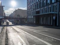 an empty street is visible in the morning sunshine with traffic driving along it and many buildings