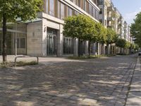 empty city sidewalk with two parked vehicles near by buildings and trees in urban setting and light blue sky