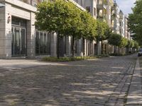 empty city sidewalk with two parked vehicles near by buildings and trees in urban setting and light blue sky