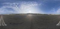 a wide angle view of the tarmac and sky with some white clouds, and the sun is shining in the distance