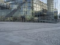 an intersection of walkway, pavement and stone in front of a large glass building on a sunny day