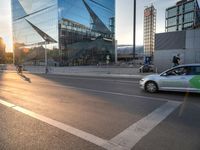 a group of cyclists riding across a street next to tall glass buildings and a car