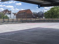 an empty parking lot on a sunny day, looking over buildings to a street corner with a bridge in front