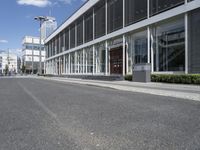 an empty street with buildings and people walking by it on a sunny day from the back