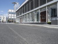 an empty street with buildings and people walking by it on a sunny day from the back