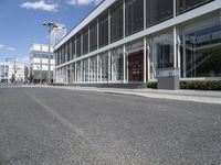 an empty street with buildings and people walking by it on a sunny day from the back