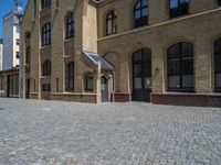 the sidewalk is paved with stones and has a bench in front of it, with no people inside