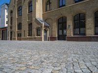 the sidewalk is paved with stones and has a bench in front of it, with no people inside