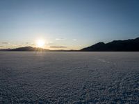 the sun shines behind the horizon as it sets in a snowy field full of snow