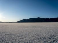 a lone snow boarder is traveling across an empty field at sunset, with the sun shining on the distant hills in the background