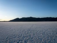 a lone snow boarder is traveling across an empty field at sunset, with the sun shining on the distant hills in the background