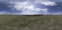 a panorama of the landscape of an open plain with clouds in the sky and grass in the foreground
