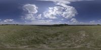 a grass covered field with an enormous cloud in the sky above it and a small hill on top in the distance