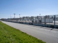 a chain link fence and a street on a sunny day at a large factory with no gates