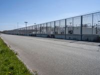 a chain link fence and a street on a sunny day at a large factory with no gates