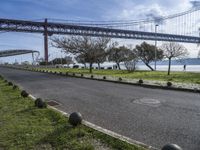 a street lined with black balls under a bridge over a body of water on a sunny day