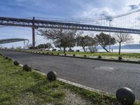 a street lined with black balls under a bridge over a body of water on a sunny day