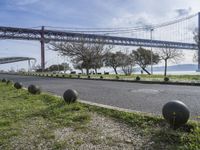 a street lined with black balls under a bridge over a body of water on a sunny day