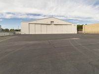 an empty parking lot in front of a building on a sunny day with clouds overhead