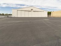 an empty parking lot in front of a building on a sunny day with clouds overhead