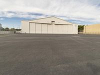 an empty parking lot in front of a building on a sunny day with clouds overhead