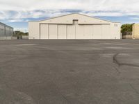 an empty parking lot in front of a building on a sunny day with clouds overhead