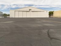 an empty parking lot in front of a building on a sunny day with clouds overhead