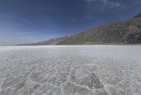 the ground is made with white sand and dry ground and mountains in the background are clouds