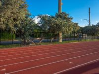 a red running track next to trees and fencing with a clock tower in the distance