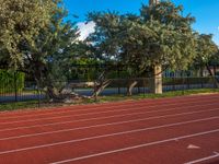 a red running track next to trees and fencing with a clock tower in the distance