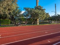 a red running track next to trees and fencing with a clock tower in the distance