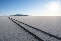 two tracks in a barren salt flat landscape with distant mountain ranges in the distance,