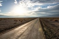 a dirt road with no cars and a bike leaning on it as the sun sets over the mountains