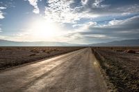 a dirt road with no cars and a bike leaning on it as the sun sets over the mountains