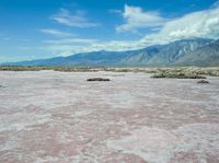 a view of the mountains in the distance with water and rocks on a flat surface