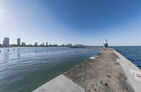 the view of a wide ocean on a sunny day with buildings in the background and a sidewalk leading to the water