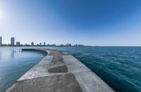 the view of a wide ocean on a sunny day with buildings in the background and a sidewalk leading to the water